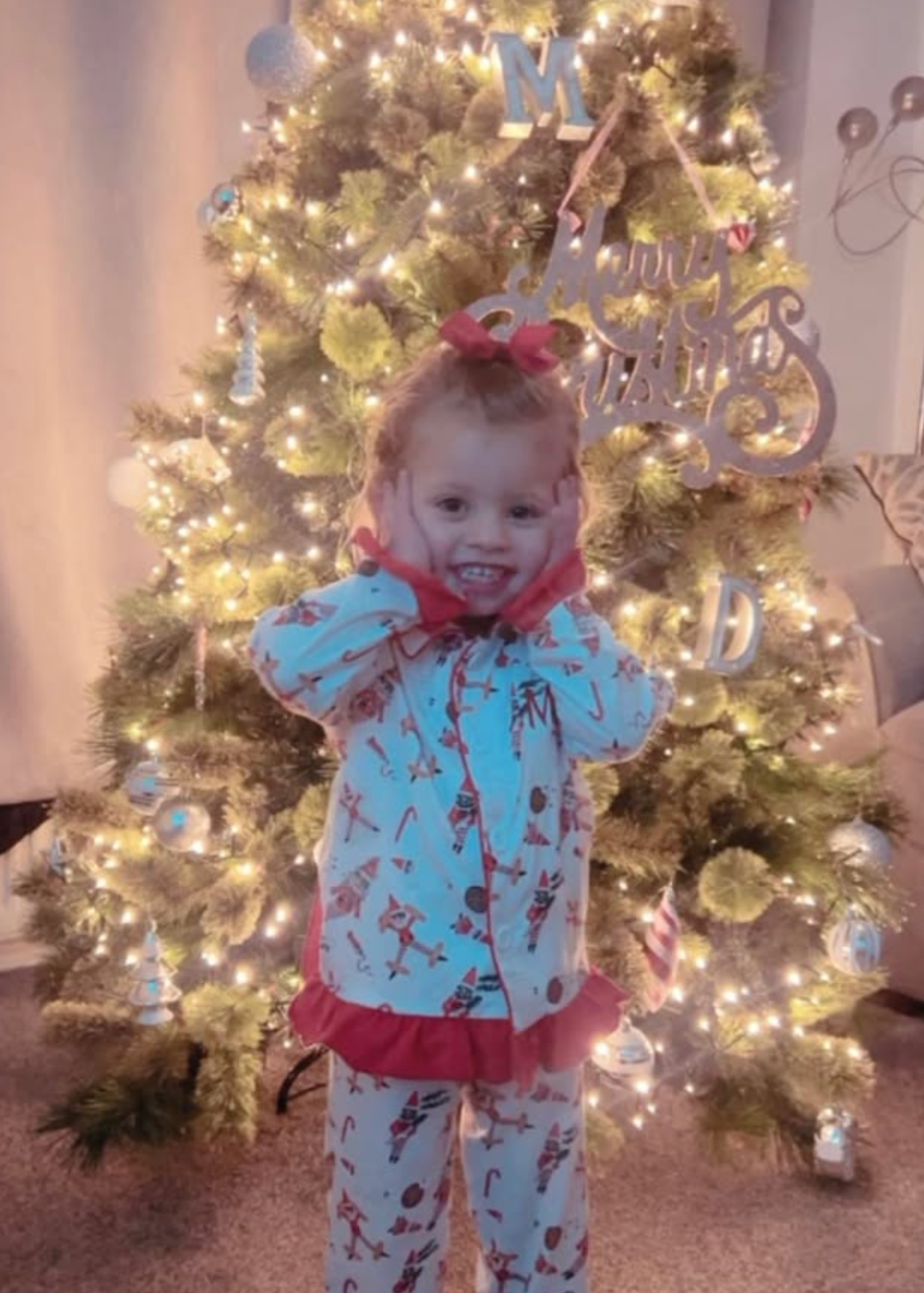 Child in pajamas standing in front of a decorated Christmas tree