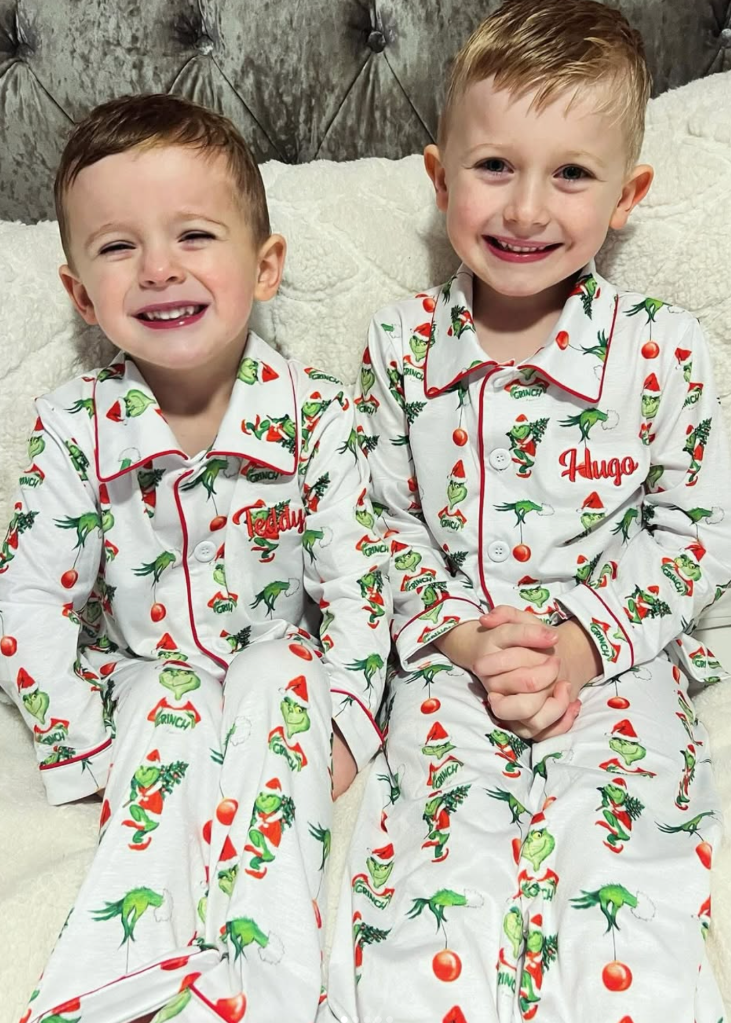 Two children wearing matching pajamas with a Christmas tree pattern on a bed.