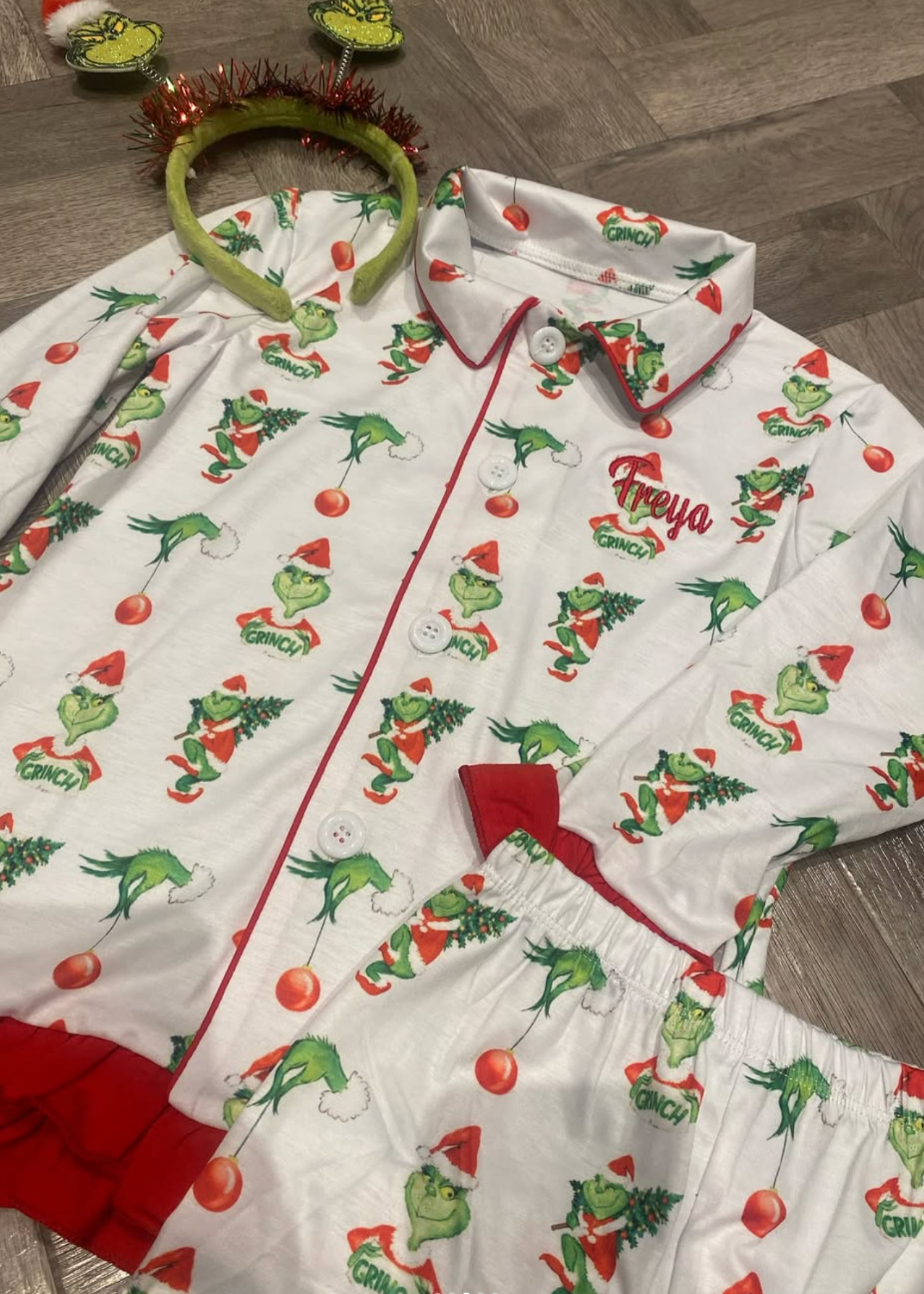 Children's Christmas-themed pajama set with Grinch print on a wooden floor.