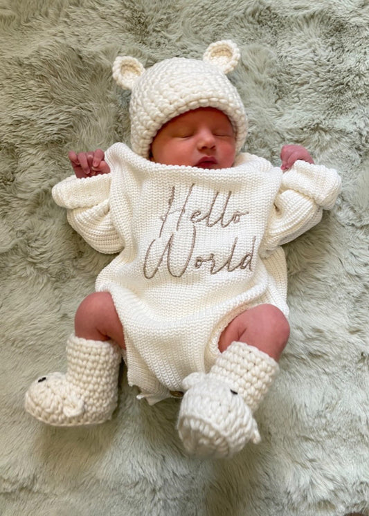 Newborn baby wearing a white knitted outfit with 'Hello World' text, lying on a fluffy surface.