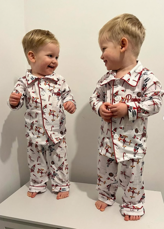 Two children wearing matching pajamas with a Christmas theme on a white surface.