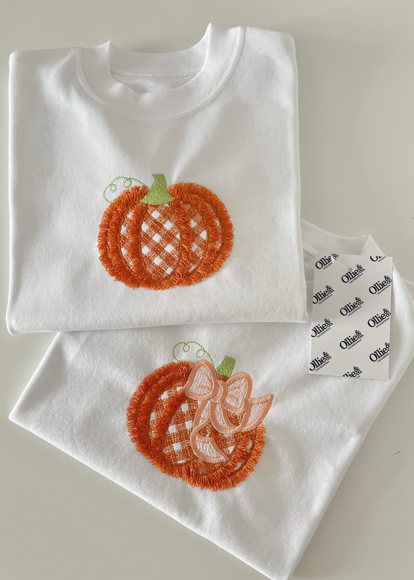 A white baby T-shirt with a fluffy pumpkin design and a matching baby romper with the same design, laid flat on a surface.