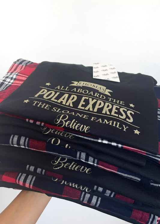 A stack of folded red and navy tartan patterned pyjamas with a short sleeve navy tee on top, all with a 'Polar Express' text design.