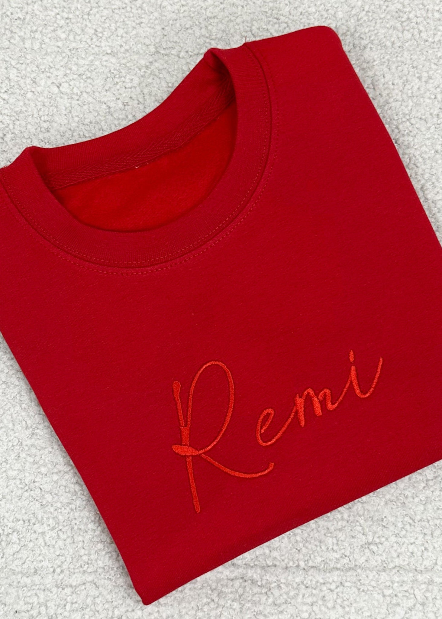 A bright red sweater with the name 'Remi' embroidered in orange on the chest area.