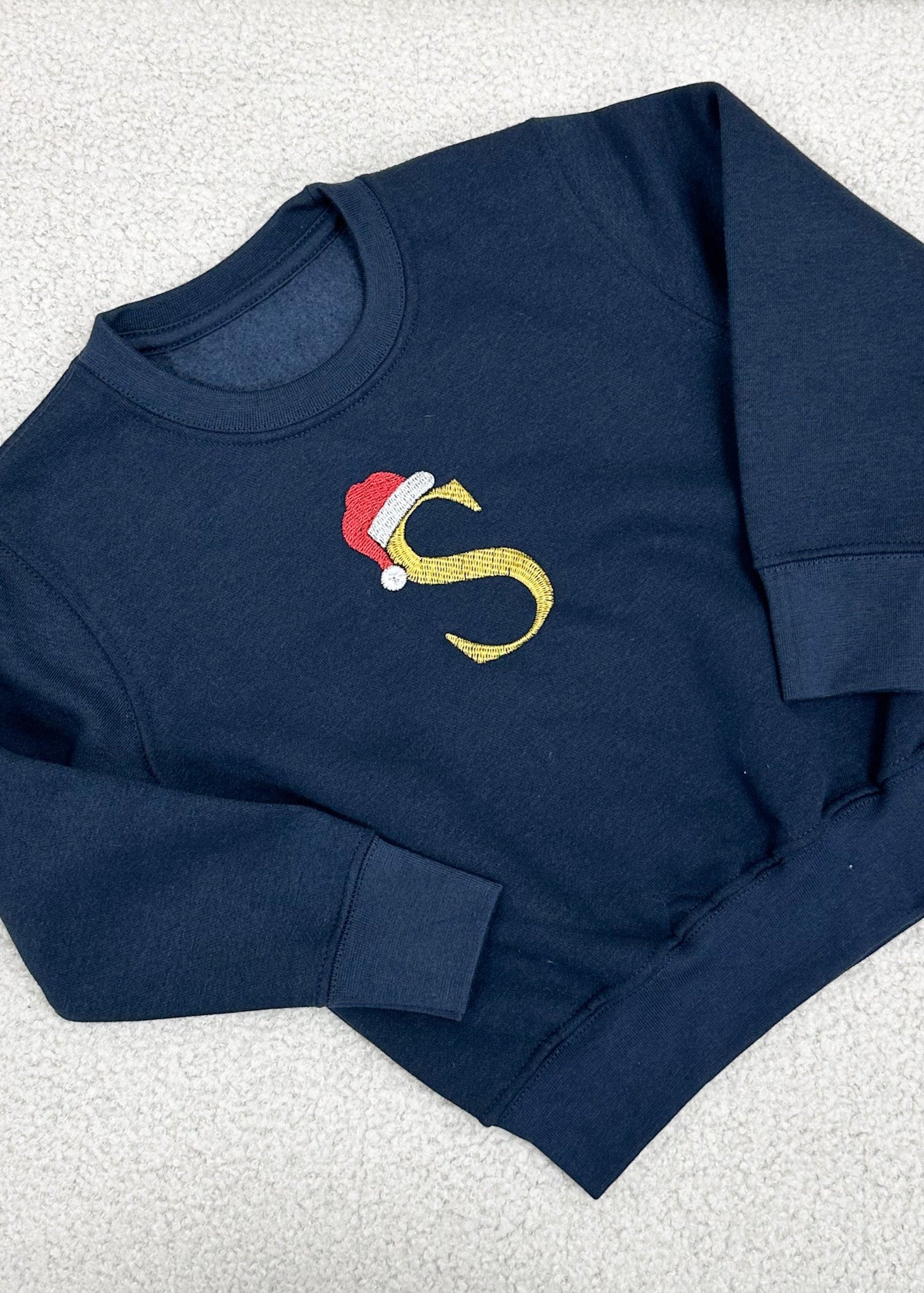 A navy blue sweater with a gold embroidered Santa hat and the letter 'S' on the front.