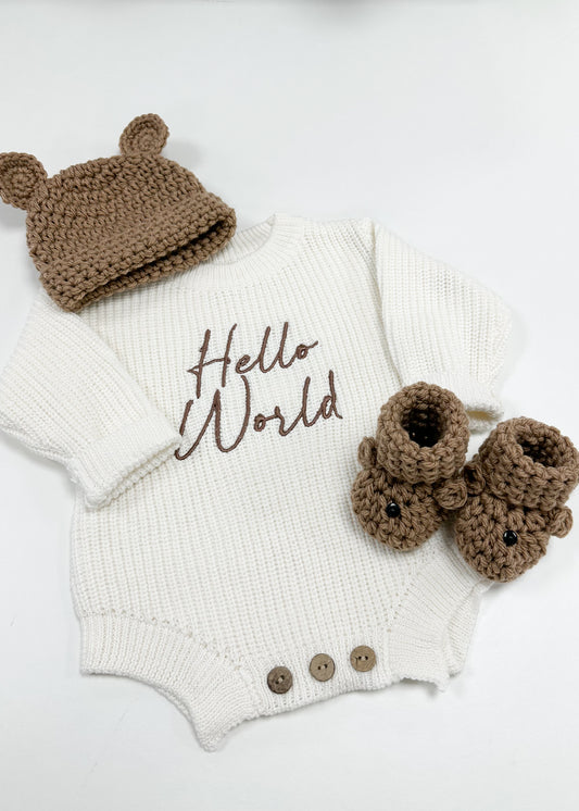 Baby outfit set with white onesie, brown hat, and booties on a light background