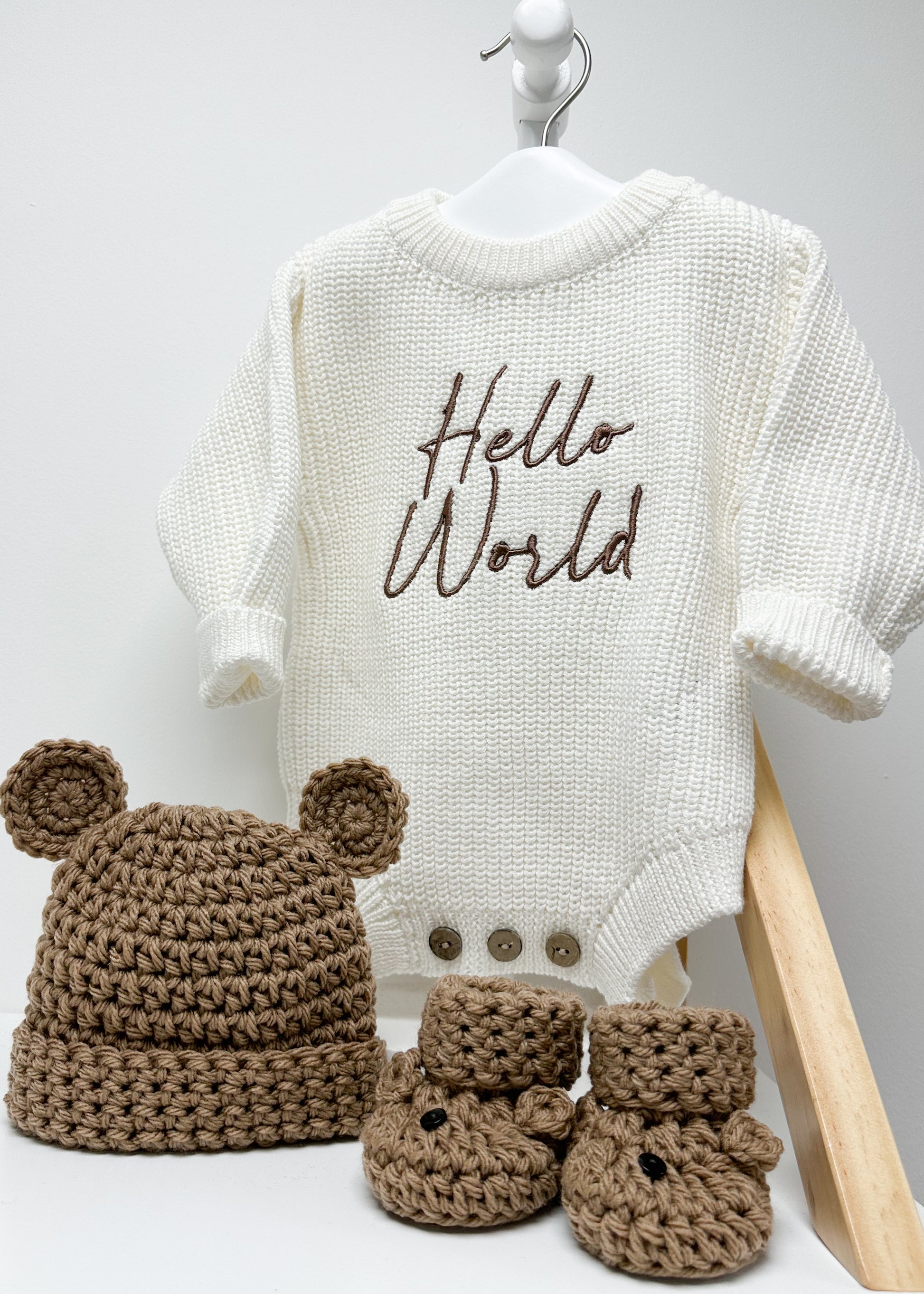Baby outfit with 'Hello World' onesie, brown hat, and boots on a white background
