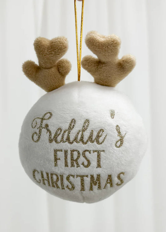 A white personalised reindeer decoration with beige antlers and the text 'Frederie's First Christmas' on it, hanging from a golden ribbon.