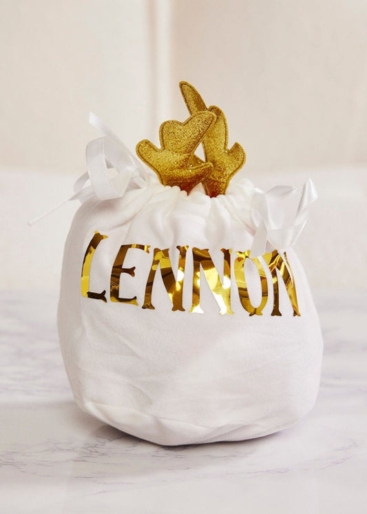 White drawstring bag with 'LENNON' printed in gold, containing gold leaf-shaped objects on a light background.