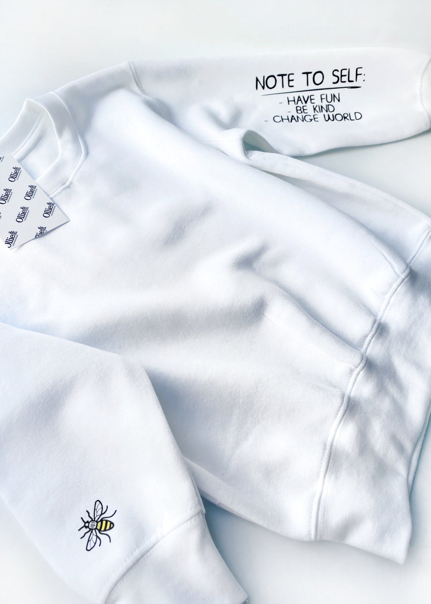 White sweater with black text on it, displayed on a flat surface.