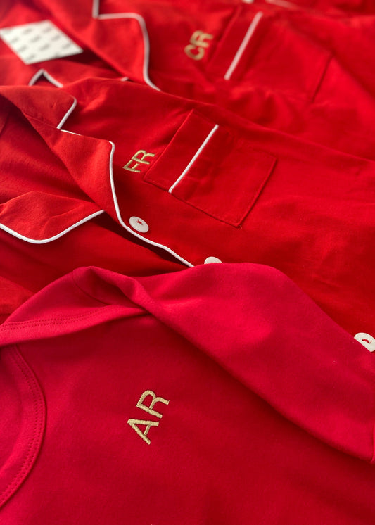 A collection of red Christmas rompers with embroidered text on the left chest, displayed in a row with visible tags.