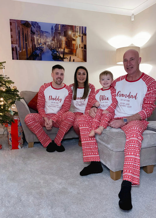 A family of four, including two adults and two children, sitting on a couch and wearing matching red and white Christmas pyjamas with a snowman design and text on the back.