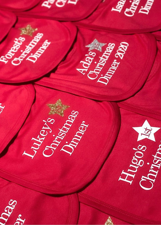 A collection of red velvet Christmas dinner bibs with white printed text and designs, including 'Turkey' and 'Christmas Dinner'.