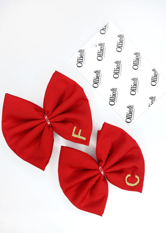 Two red hair bows with white text on them, one displayed in front and the other in the back, against a white background.