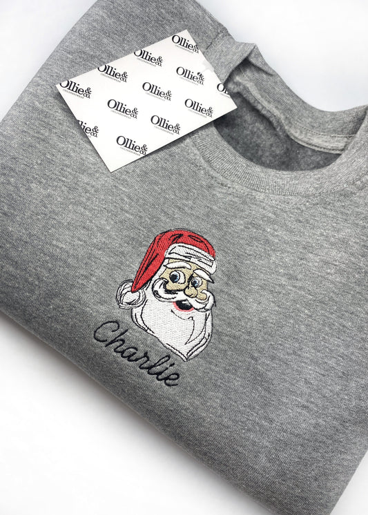 Grey sweater with a Christmas themed graphic of Santa Claus on the front, with the brand name 'Ollie' on the tag.