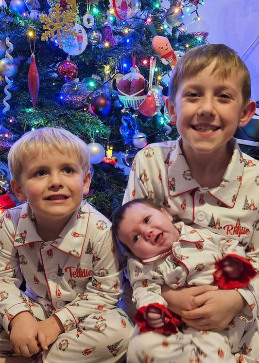 Three children in matching pajamas standing in front of a decorated Christmas tree.