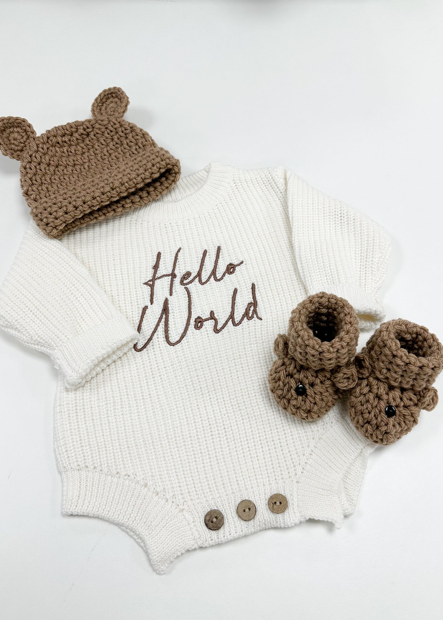 Baby outfit set with white onesie, brown hat, and booties on a light background