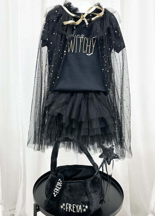 Black Halloween costume with cape, skirt, and bag on a stand against a white curtain background.